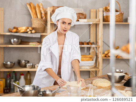 Seductive female chef kneading dough in rustic bakery Seductive female chef kneading dough in rustic bakery 126089521