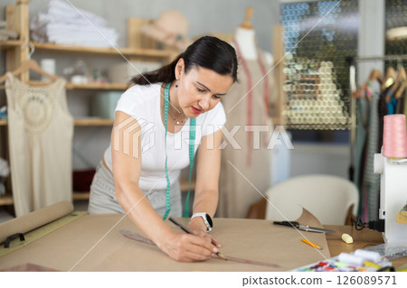 Woman dressmaker drawing pattern on paper in workshop 126089571