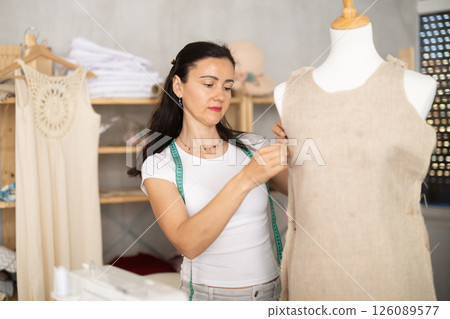 Woman tailor connects parts of dress on mannequin Woman tailor connects parts of dress on mannequin 126089577