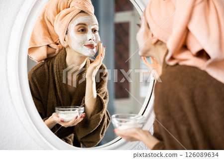 Woman smoothing face cream in front of mirror Woman smoothing face cream in front of mirror 126089634