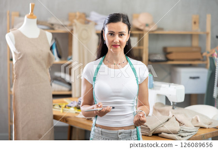 Woman seamstress posing in sewing workshop Woman seamstress posing in sewing workshop 126089656