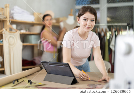 Girl tailor draws pattern on a sheet of paper in sewing workshop 126089665