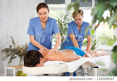 Two professional masseuses performing back massage for male patient 126089697