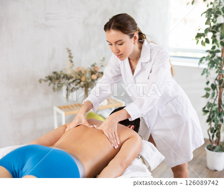 Professional young masseuse performing back massage for male patient Professional young masseuse performing back massage for male patient 126089742