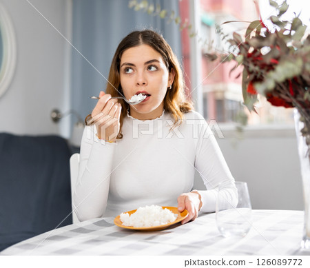 Woman sitting at table and eating boiled rice at home Woman sitting at table and eating boiled rice at home 126089772
