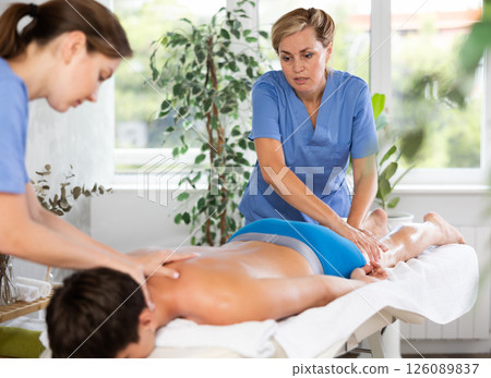 Masseuse with female assistant performing four hands massage to man 126089837