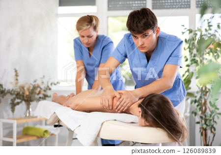 Professional masseur and masseuse performing back massage for female patient 126089839