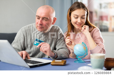 Happy married couple book a vacation tour on a laptop 126089864