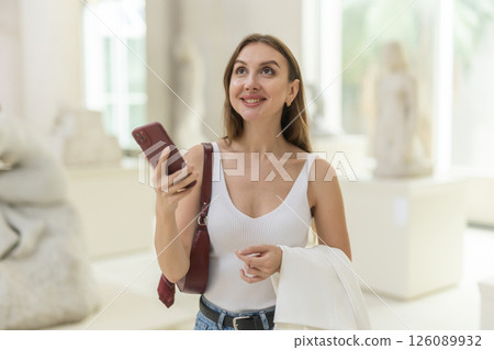 While visiting museum, girl uses travel guide application on her phone. While visiting museum, girl uses travel guide application on her phone. 126089932