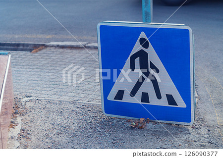 A road sign indicating a place for a pedestrian crossing slid down onto the sidewalk. The symbolism of a visual representation of how pedestrians should cross the road A road sign indicating a place for a pedestrian crossing slid down onto the sidewalk. The symbolism of a visual representation of how pedestrians should cross the road 126090377