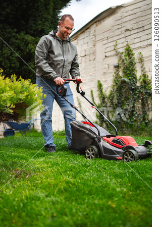 Lawn care enthusiast practices weekend gardening with electric mower in a well-kept yard Lawn care enthusiast practices weekend gardening with electric mower in a well-kept yard 126090513