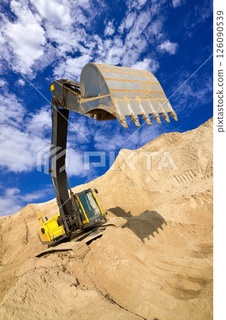 Heavy Excavator Digging Sand at Construction Site Under Blue Sky 126090539