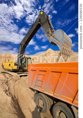 Excavator Loading Sand into Dump Truck at Quarry Site 126090550