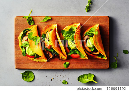 Mini crepes filled with cashew cream, spinach, and fried mushrooms, presented in a minimalist style. The natural colors of the ingredients create a vibrant and fresh look 126091192