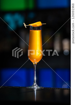 A vibrant orange cocktail is served in a tall, slender glass, garnished with a thin slice of orange peel skewered across the rim. 126091968