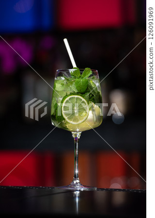 A refreshing green Mojito cocktail, filled with mint leaves, lime slices, and ice, is served in a tall glass with a white straw. A refreshing green Mojito cocktail, filled with mint leaves, lime slices, and ice, is served in a tall glass with a white straw. 126091969
