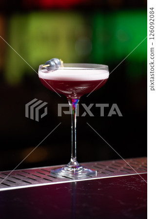 purple cocktail with a foamy white top is garnished with skewered blueberries on a textured bar surface 126092084