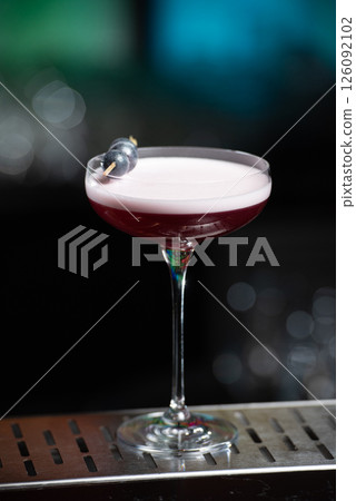 purple cocktail with a foamy white top is garnished with skewered blueberries on a textured bar surface purple cocktail with a foamy white top is garnished with skewered blueberries on a textured bar surface 126092102