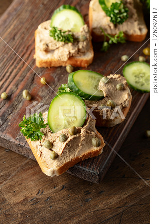 Open sandwiches with pate, cucumber, capers, and parsley on a old cutting board. Open sandwiches with pate, cucumber, capers, and parsley on a old cutting board. 126092612