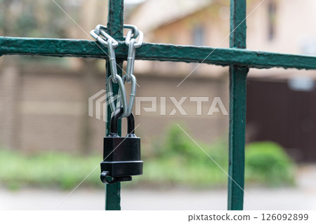 Close-up of black padlock and chain on metal gate. 126092899