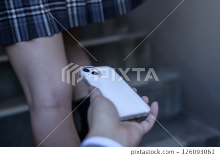 A man's hand taking a secret photo of a high school girl walking up the stairs while holding down her skirt 126093061