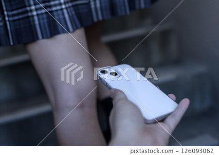 A man's hand taking a secret photo of a high school girl walking up the stairs while holding down her skirt 126093062