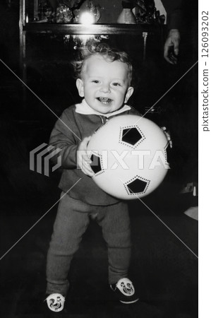 Vintage portrait of a curly little boy holding a ball in his hands. The child is learning to walk. The boy is smiling. Retro photo from 1967. Vintage portrait of a curly little boy holding a ball in his hands. The child is learning to walk. The boy is smiling. Retro photo from 1967. 126093202
