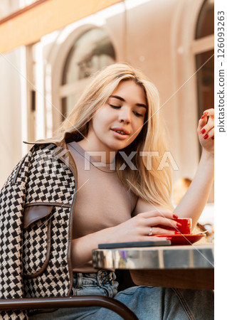 Woman Coffee Cafe - Blonde woman sits at a cafe table, enjoying a cup of coffee in a European city. 126093263