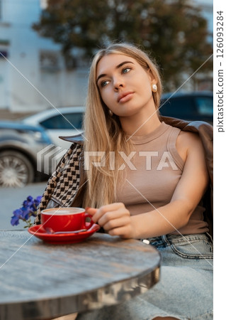 Woman Coffee Cafe - Young woman enjoying a cup of coffee while sitting at an outdoor cafe table. Woman Coffee Cafe - Young woman enjoying a cup of coffee while sitting at an outdoor cafe table. 126093284