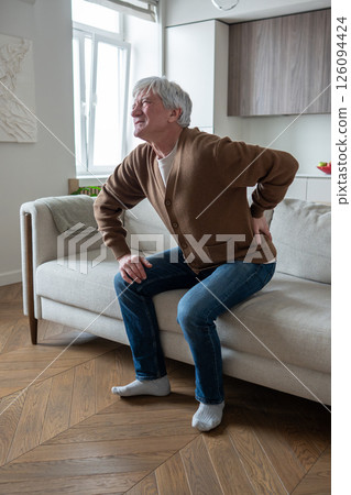 Sad depressed senior man suffering from osteochondrosis barely stand up from sofa, acute back pain Sad depressed senior man suffering from osteochondrosis barely stand up from sofa, acute back pain 126094424