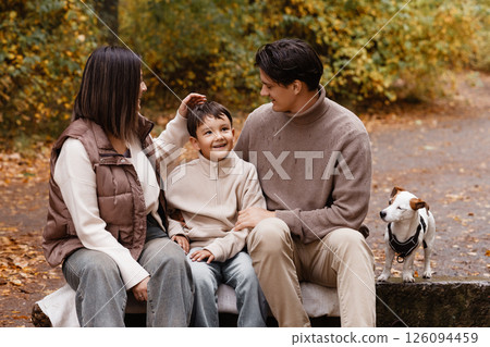 Happy family of three with dog sitting on bench in autumn park Happy family of three with dog sitting on bench in autumn park 126094459