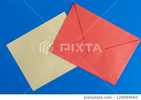 Bright red envelope with paper on a blue background surface. 126094660