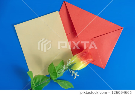 Red envelope with a blank card and an artificial flower on a blue background for Valentine's Day. 126094665