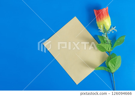 Colorful artificial rose flower and yellow paper blank card on dark blue background. 126094666