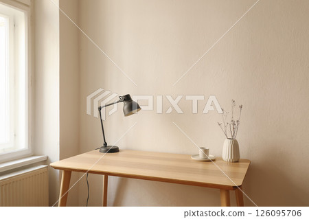 Elegant Scandinavian interior, living room. Modern grey lamp on bamboo desk, table. Dry flowers in vase. Cup of coffee, tea. Trendy working space, home office. Beige wall background, copy space. 126095706