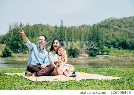 Asian family father mother and daughter sitting on blanket spring meadow field grass sunny day in park cheerful sweet kid girl, parents and child picnic enjoying outdoors together, Family relaxation 126096496