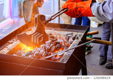 Blacksmith shapes heated metal with tongs, surrounded by glowing coals at craft during axe making 126096629