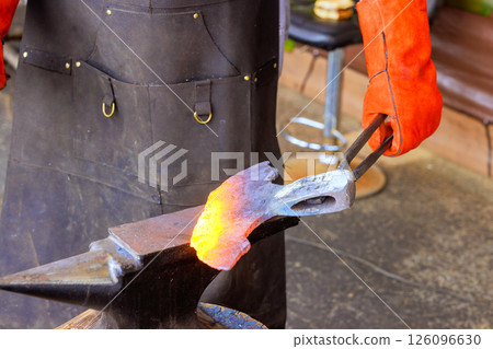 Skilled artisan forges glowing metal into tool, showcasing traditional craftsmanship axe making 126096630