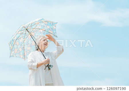 A senior woman walking with a parasol under the blue sky A senior woman walking with a parasol under the blue sky 126097190