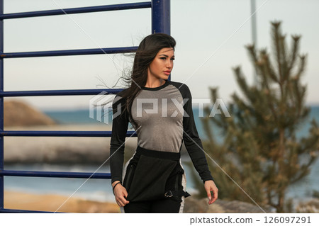 woman dressed in fitted long sleeve shirt and athletic pants walks confidently along waterfront enjoying the ocean breeze and scenic surroundings during her workout. woman dressed in fitted long sleeve shirt and athletic pants walks confidently along waterfront enjoying the ocean breeze and scenic surroundings during her workout. 126097291