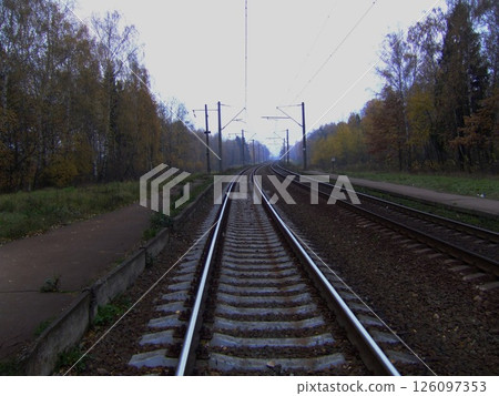 Curved railway tracks disappearing into the distance through an autumn forest with overhead electrical lines and an empty rural platform. High quality photo Curved railway tracks disappearing into the distance through an autumn forest with overhead electrical lines and an empty rural platform. High quality photo 126097353