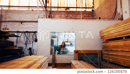 Woman, phone call and talk at warehouse for wood, order or stock for construction material at plant. Person, smartphone and inventory with timber for manufacturing, storage or production at factory 126100870