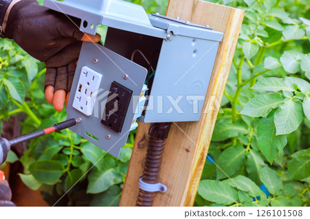 Electrician connects electrical components to box mounted outlet, USB ports on wooden post 126101508