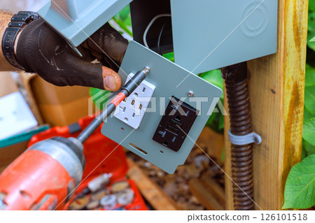 Electrician works on installing power outlet with USB ports in garden setting amid greenery. Electrician works on installing power outlet with USB ports in garden setting amid greenery. 126101518