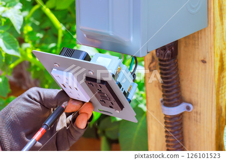 Electrician worker connects an outdoor outlet, USB ports to provide electrical access in garden setting. Electrician worker connects an outdoor outlet, USB ports to provide electrical access in garden setting. 126101523