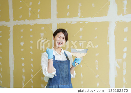 A woman doing DIY applying putty to plasterboard A woman doing DIY applying putty to plasterboard 126102270