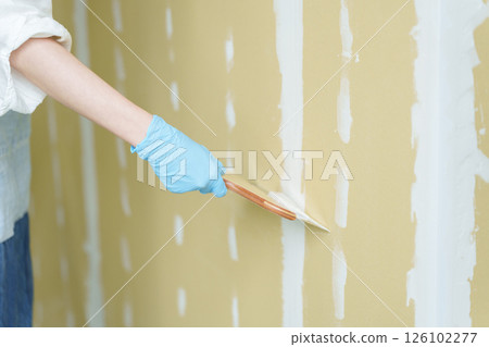 A woman doing DIY applying putty to plasterboard A woman doing DIY applying putty to plasterboard 126102277