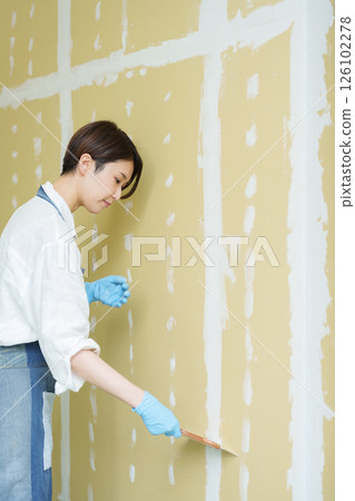 A woman doing DIY applying putty to plasterboard A woman doing DIY applying putty to plasterboard 126102278