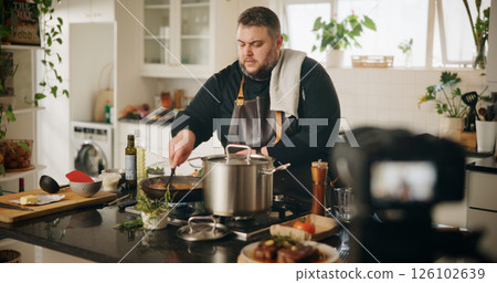 Home, cooking and man with live streaming in kitchen for dinner tutorial, food vlog and video recording. Culinary influencer, content creation and person with cuisine instructions or meal preparation 126102639