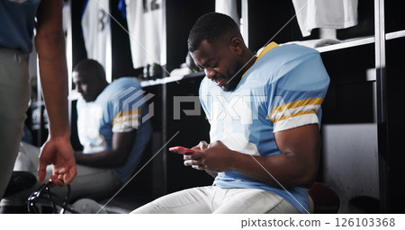 Football, player and texting with phone in locker room for message response, check notifications and game break. Sports, man and relax with smartphone for social media, online news and web connection 126103368